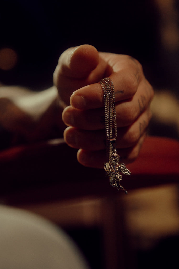 hand holding a chain with an angel pendant on it.