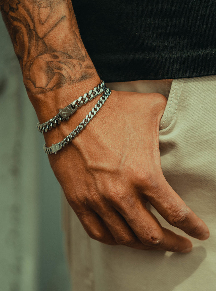 a mans hand with his thumb in his pocket, wearing two platinum cuban link bracelets.
