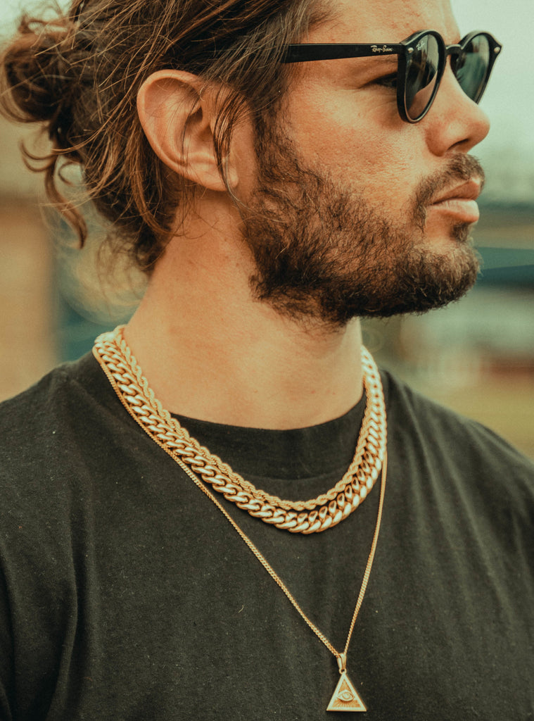 man wearing a gold cuban chain, gold rope chain and pendant. ALso wearing sunglasses and looking to the right.