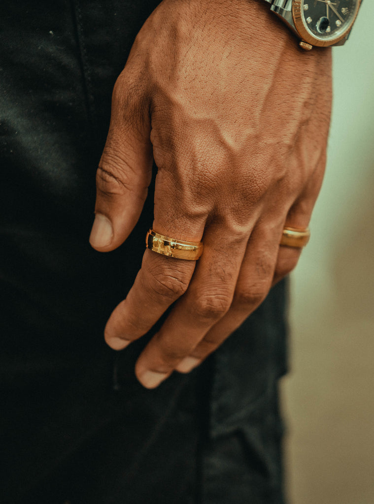 a mans hand in a watch and two gold rings.