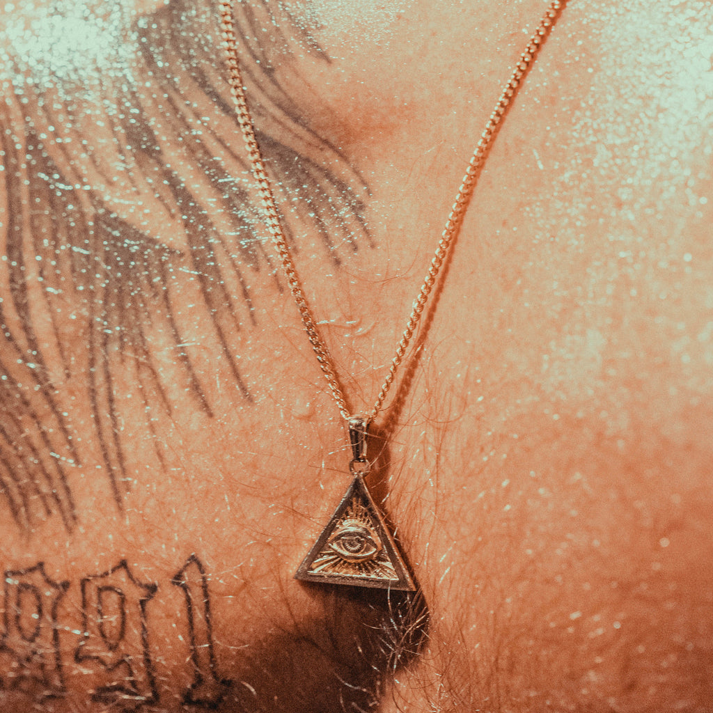 Gold pendant in an illuminati triangle on a man's chest.